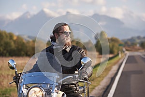 Bearded biker in black leather jacket on modern motorcycle on country roadside.