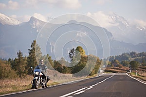 Bearded biker in black leather jacket on modern motorcycle on country roadside.