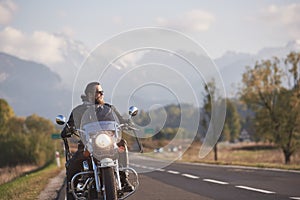 Bearded biker in black leather jacket on modern motorcycle on country roadside.