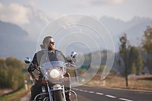 Bearded biker in black leather jacket on modern motorcycle on country roadside.