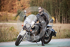 Bearded biker in black leather jacket on modern motorcycle on country roadside.