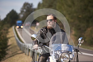 Bearded biker with long hair in black leather jacket sitting on modern motorcycle.