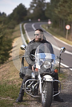 Bearded biker with long hair in black leather jacket sitting on modern motorcycle.