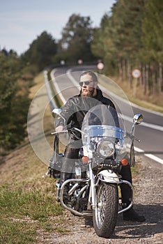 Bearded biker with long hair in black leather jacket sitting on modern motorcycle.