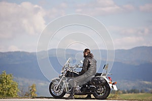 Bearded biker with long hair in black leather jacket and sunglasses sitting on modern motorcycle.