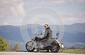 Bearded biker with long hair in black leather jacket and sunglasses sitting on modern motorcycle.