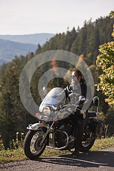 Bearded biker with long hair in black leather jacket and sunglasses sitting on modern motorcycle.