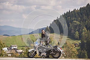 Bearded biker with long hair in black leather jacket and sunglasses sitting on modern motorcycle.