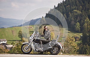 Bearded biker with long hair in black leather jacket and sunglasses sitting on modern motorcycle.