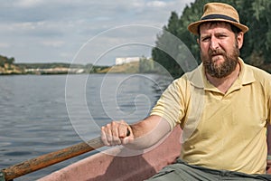 Bearded boatman in a hat on the river in a boat