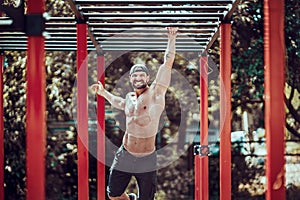 Bearded bodybuilder man exercising on monkey bars for the upper-body in a modern calisthenics park outdoors on a sunny