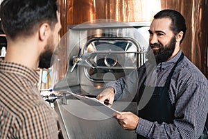 Bearded brewers inspect equipment of brewery for production of craft beer. Brewing. Brewery.
