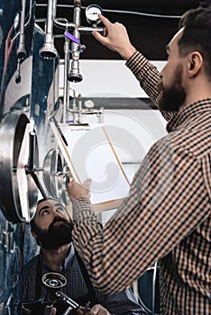 Bearded brewery worker takes readings from brewing equipment. Brewing. Brewery. Beer crafting.