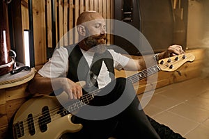 Bearded brutal guitarist tuning his musical instrument while sitting on floor