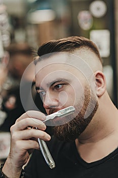 Bearded brutal man with a straight razor