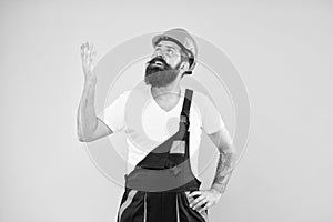 Bearded builder in hard hat and work uniform look up yellow background, construction