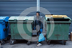 Bearded bum searching food in trashcan on street