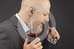 Bearded business man enjoys listening to his favorite music from an audio player with small headphones. audiophile and music lover