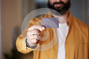 Bearded business man holding hand empty black business card on blurred background. Mockup Copy Paste Blank Advertisement