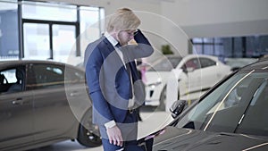 Bearded businessman choosing car in dealership close up. Tall man running hand through hair near automobile in auto show