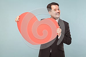 Bearded businessman holding big red heart and toothy smiling