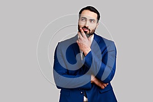 Bearded businessman holding his chin with hand, pondering about future, planning strategy.