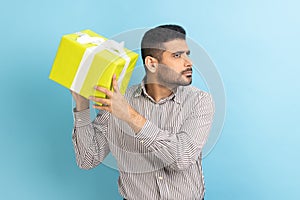 Bearded businessman holding and shaking wrapped present box, being interested what inside.