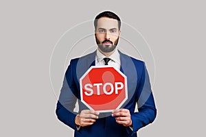 Bearded businessman holding Stop road traffic sign as symbol of prohibition, restrictions.