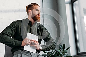 bearded businessman holding tablet and looking