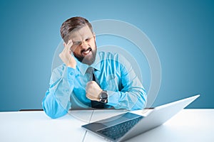 Bearded businessman at a laptop leaned his hand to his head he has severe headaches, a man sitting in the office at a computer