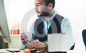 Bearded businessman looking in monitor computer at home workplace. man drinking coffee working at social distance, consultant