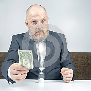 Bearded businessman offers payment for work with money against the background of the hourglass. concept of value of time to pay