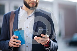 Bearded businessman reading e-mail on phone and holding coffee cup