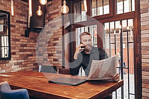Bearded businessman  talking on a mobile phone while reading newspapers