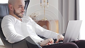 Bearded businessman working at home sitting in armchair and using computer technologies. Business, freelance and stock