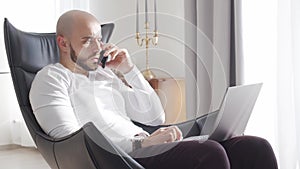 Bearded businessman working at home sitting in armchair and using computer technologies. Business, freelance and stock