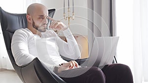 Bearded businessman working at home sitting in armchair and using computer technologies. Business, freelance and stock