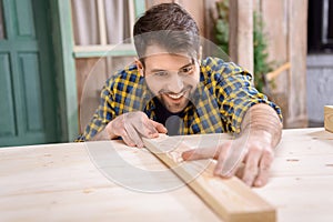 Bearded carpenter measuring wooden plank on table
