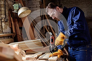 bearded carpenter in protective gloves and googles using electric drill photo