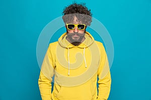 Bearded casual man wearing yellow hoodie and sunglasses confidently posing