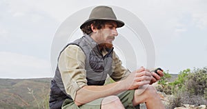 Bearded caucasian male survivalist sitting on mountain, holding compass and looking around