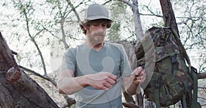 Bearded caucasian male survivalist untying paracord at camp in wilderness