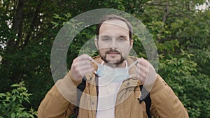 Bearded caucasian man gladly removes a protective medical mask and wearing it again.