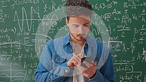 A bearded Caucasian man stands near the school blackboard. Teacher with smartphone. Communication in social networks