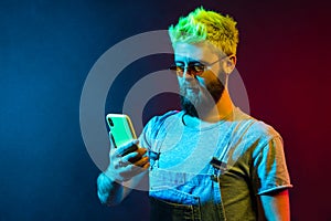 Bearded concentrated hipster man holding cell phone in hands, checking social networks, writing new post, has serious expression,