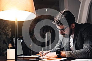 Bearded coworker working by the wood table with laptop. Creative business man make new startup at night loft office. Using modern