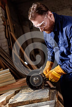 bearded craftsman in protective googles and gloves using grinding machine