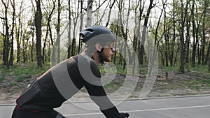 Bearded cyclist pedaling on bicycle wearing black sports outfit, helmet and glasses. Cycling concept.