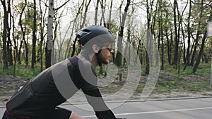 Bearded cyclist pedaling on bicycle wearing black sports outfit, helmet and glasses. Cycling concept. Slow motion