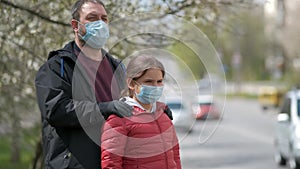 A bearded dad adjusts his daughter`s medical mask on the street of a European city . The concept of protection from COVID-19